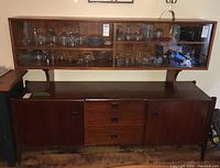 Frontal view of teak sideboard base with overhead glass-fronted hutch containing glassware