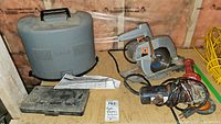 Photo showing Ryobi plastic carrying case, Black & Decker router bit metal case, circular saw, and vintage angle grinder on a wooden surface.