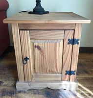 Photo showing one pine side table with paneled door, black strap hinges, ring pull handle and visible wood grain.