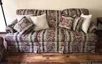 Front view of floral fabric Sears sofa showing three removable seat cushions and multiple accent pillows on a wooden floor.