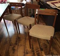 Three teak dining chairs positioned in front of a storage cabinet showing overall design