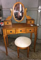 Wooden vanity with oval mirror mounted and four knobs on drawer fronts, placed in a garage setting.