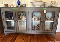 Full frontal view of the grey wood display cabinet with four glass front doors showing internal shelves and decorative items inside.