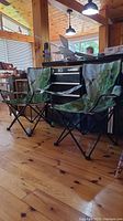 Two matching folding camp chairs with vibrant hummingbird and greenery pattern on canvas fabric, black metal foldable frames, placed indoors on wooden floor.