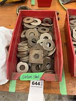 Red plastic container holding numerous assorted carbon steel washers, both round and square.