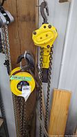 Yellow Power Fist 2 ton manual chain hoist with hook hanging on wire rack next to other chains.