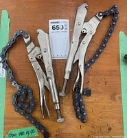 Two metal chain vice grips with attached chains, placed on a wooden surface. One grip shows clear stamping 'The Original Since 1924 Made in USA'.
