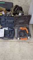 Photo showing the orange 3/8" drill and the black and blue drill in their cases with cords visible.