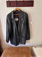 Full view of black leather jacket hanging on a wooden hanger, showing front details and two buttons