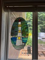 Stained glass lighthouse light catcher hanging in window showing entire piece with natural background.