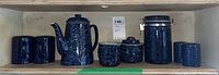 Front view of blue speckled ceramic serving kettle, canisters, salt and pepper shakers, creamer, and sugar containers arranged on wooden shelf