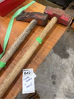 Top down view of sledgehammer and maul side by side on wooden surface showing tool heads and handles.