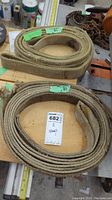 Two rolled tow ropes or slings with green tags indicating lengths, lying on wooden surface with other tools.