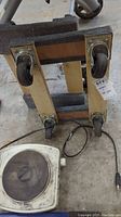 Photo showing bottom of wooden trolley with four caster wheels and portion of electric hot plate cord