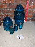 Front view of the set showing all five items with lids and shakers on a cloth surface against a brick wall.