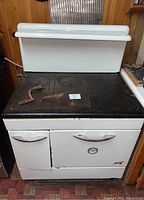 Front view of the antique Majestic wood and coal range showing the white enamel body, chrome handles, and cast iron cooktop with four burner covers and two metal tools.