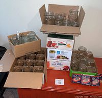 Boxes of glass canning jars and Ball brand mason jar lids on a wooden table.