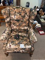 Front view of vintage wingback chair showing floral and equestrian upholstery