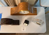 Top view showing all four clocks arranged on a white table: large oak Howard Miller mantle clock, dark polished wooden Seahawk emblem clock, travel clock, and clear Mikasa crystal clock.