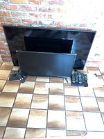 Photo shows 50 inch Samsung TV and 32 inch Insignia TV placed on floor with their remote controls and some remote controls stacked beside them.