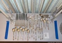 Overall view of complete silver plated flatware set arranged with crystal candlesticks on white tablecloth.