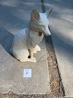 Concrete fox statue sitting on a sidewalk, shown from front angle