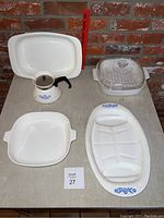 Photo of all five Corning Ware pieces including baking dishes, coffee pot, and serving tray on beige surface with brick background.