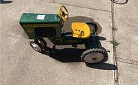 Full side view of green and yellow Fleetwing pedal tractor toy, showing metal body with decals, yellow seat and steering wheel, and three wheels.