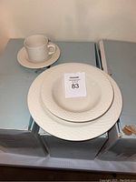 Display of cup, saucer, cereal bowl, and dinner plate with boxes underneath
