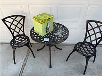 Full lot showing black metal lattice round table approx 26" height 23" diameter, two matching lattice metal chairs 32" height, gazing ball box, concrete pig ornament on table