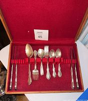 Top view of the complete set of Towle sterling silverware in open red velvet-lined wooden case showing various sizes and styles of spoons, forks, and chopsticks.