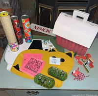 Wide view of vintage children collectibles on table including kaleidoscopes, animal figurines, miniature tea set, cat placemat, and Peanuts cook book.
