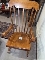 Front view of vintage colonial style solid wood rocking chair showing the tall back with vertical slats and curved armrests.