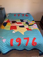 Full view of the vintage quilt spread on a bed showing "1776" at the top and "1976" at the bottom with patchwork in the center.