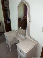 Side angled view of the vintage Karpen vanity showing its painted finish, arched mirror, and two drawer stacks with carved details and ring pulls.