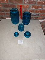 Full set of the three aqua blue glass canisters and two lids with a measuring ruler for scale