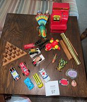 Photo of all 23 metal tin toys and wood peg game pieces arranged on a wood table, showing variety of vintage toys including tin cars, animals, and kaleidoscope.