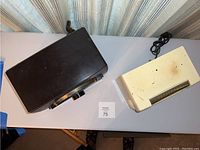 Two vintage radios on a white table; one black General Electric box-shaped radio and one white rectangular bakelite radio with horizontal AM frequency display.