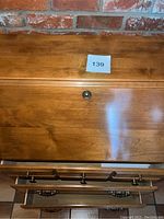 Closed view of the fold-down writing surface with a keyhole at the center and wood grain visible.