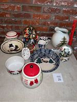 View of the full collection of Christmas themed items against a brick background showing bowls, pitchers, figurines and snow globes.