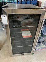 Front view of stainless steel bar cooler with glass door showing interior wire shelves and instruction booklet inside.