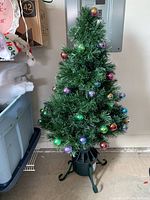 Artificial small Christmas tree decorated with multicolored ball ornaments standing on black plastic tree stand