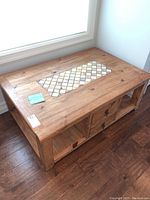 Photo of light coloured wooden coffee table showing tile inlay at center and storage drawers underneath
