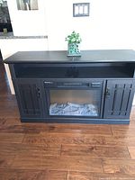 Full frontal view of the MasterFlame electric fireplace console showing the black wooden frame, panel doors on each side, and electric fireplace insert with logs visible inside.