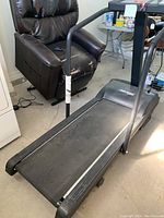 Photo showing overall treadmill with running belt, side rails, and part of nearby recliner chair.