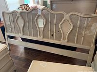 Front perspective view of the French Provincial style king size headboard showing the curved top rail, central shaped panels, and woven cane inserts in a brushed white finish.