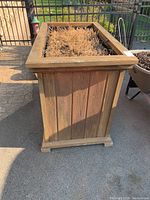 Front side view of large wooden garden container with soil and dried plants inside