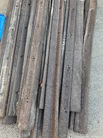 Top view of stacked dark brown rubberized garden edging strips with evenly spaced holes for pegs, showing some surface wear and dirt.
