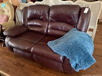 Full view of brown leather-like loveseat recliner with manual reclining feature, blue throw blanket on seat, showing condition and design.