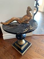Side table showing round black marble top with gold veining, black and gold base, and decorative gold bird sculpture on top.